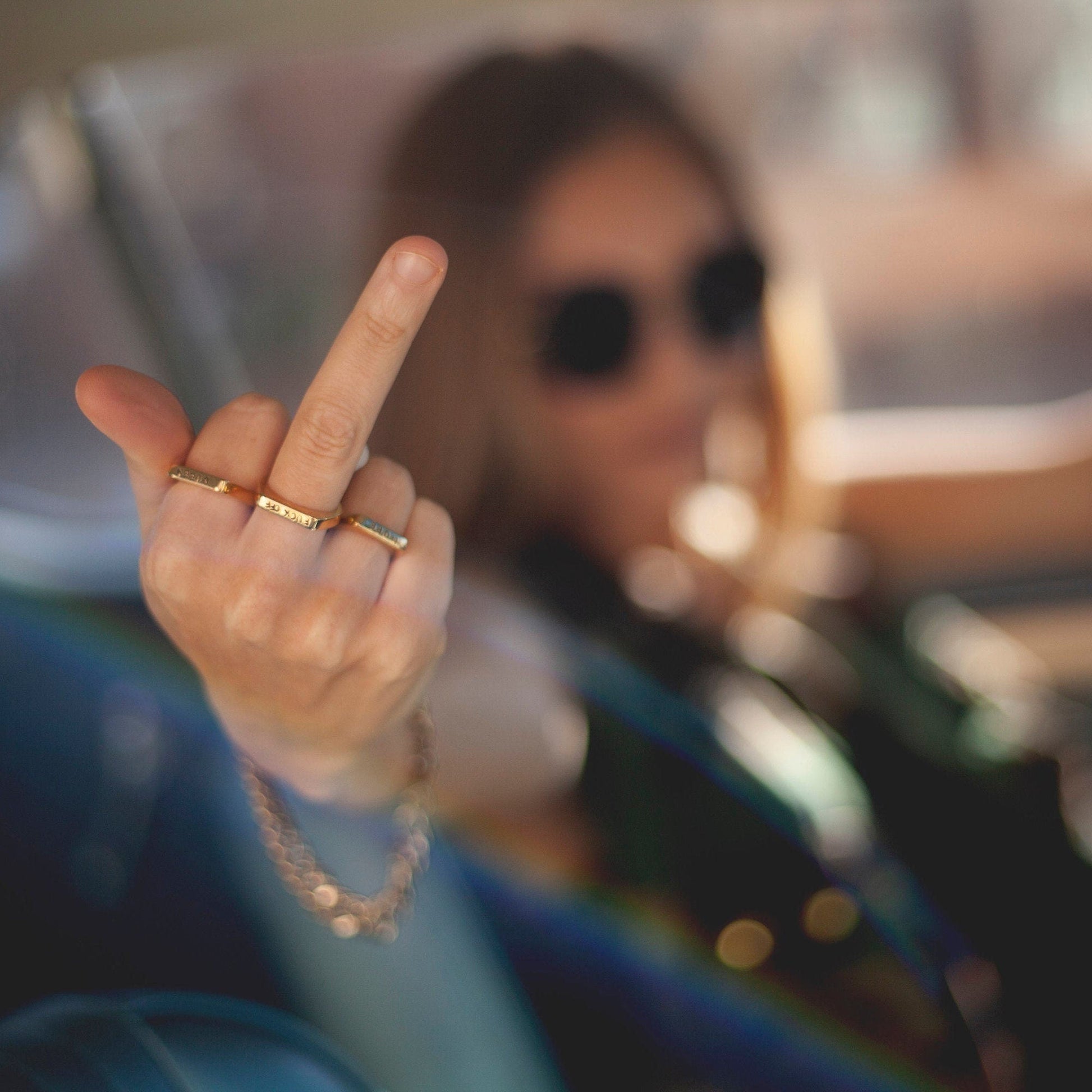 Person wearing sunglasses and a gold ring, with a blurred background