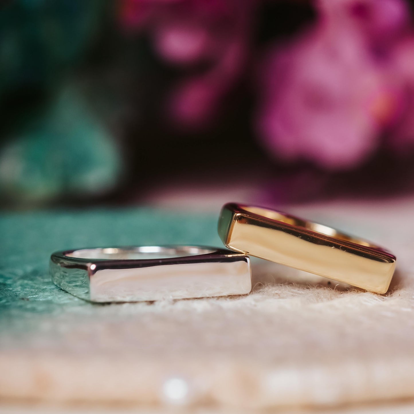 Gold and silver rings on a textured surface with blurred floral background