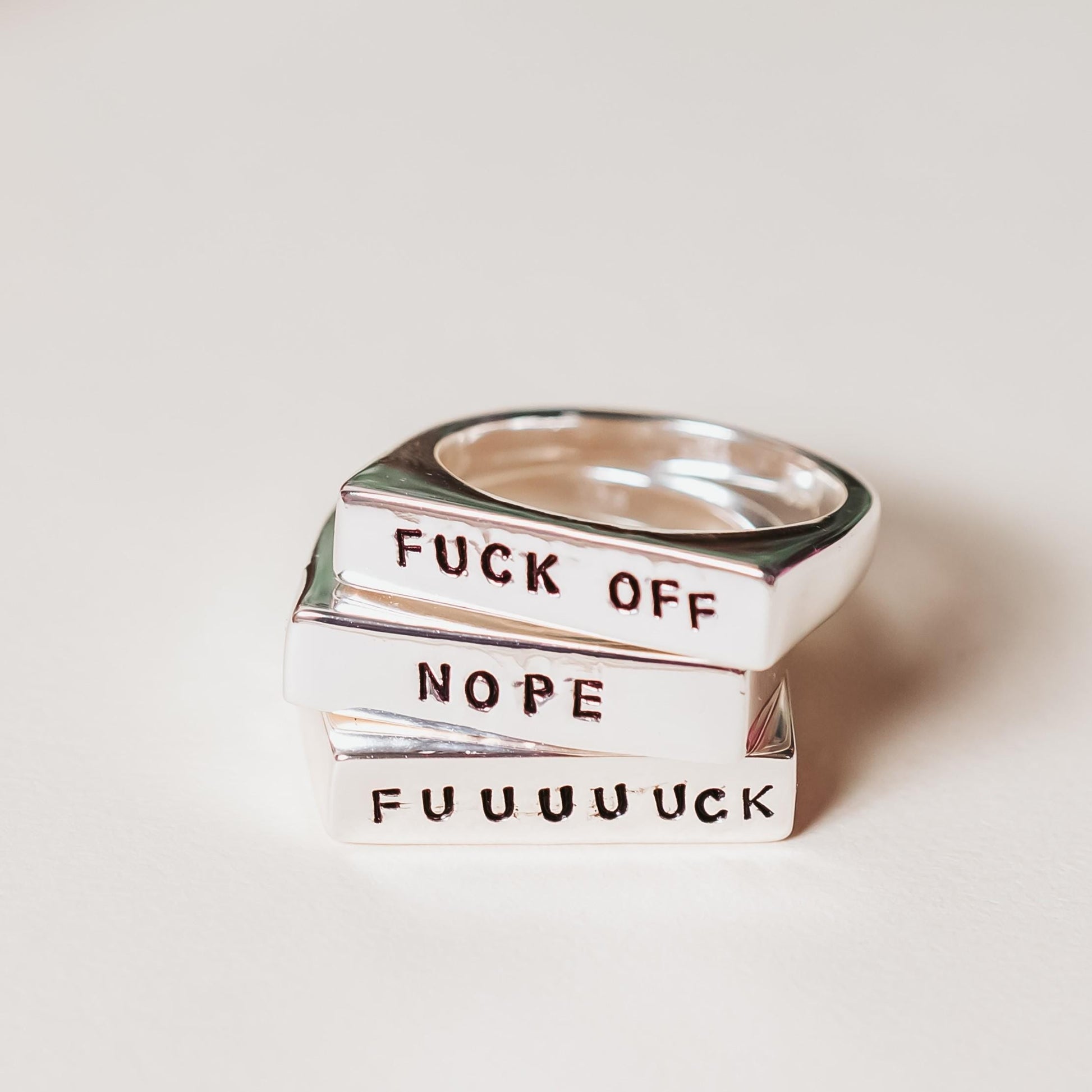 Silver ring with text 'FUCK OFF', 'NOPE', and 'FUUUUUCK' on a light background