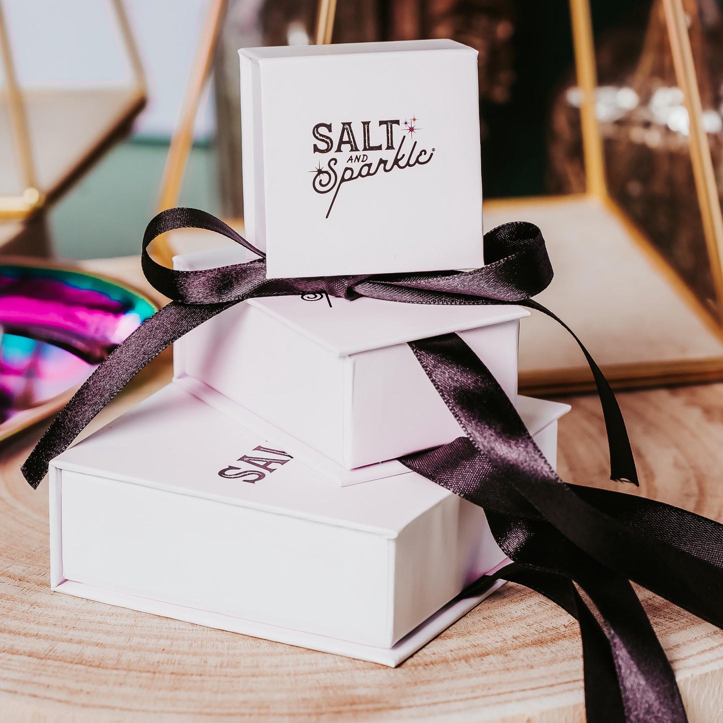 White jewelry box with 'Salt & Sparkle' branding and a black ribbon on a wooden surface.