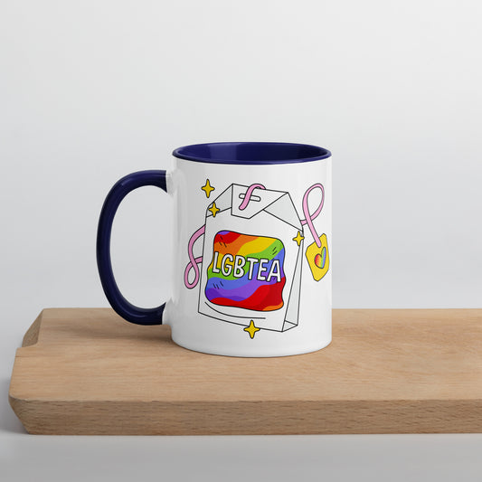 White ceramic LGBTea mug with dark blue handle and interior, featuring a rainbow tea bag illustration with pink ribbons and sparkles.