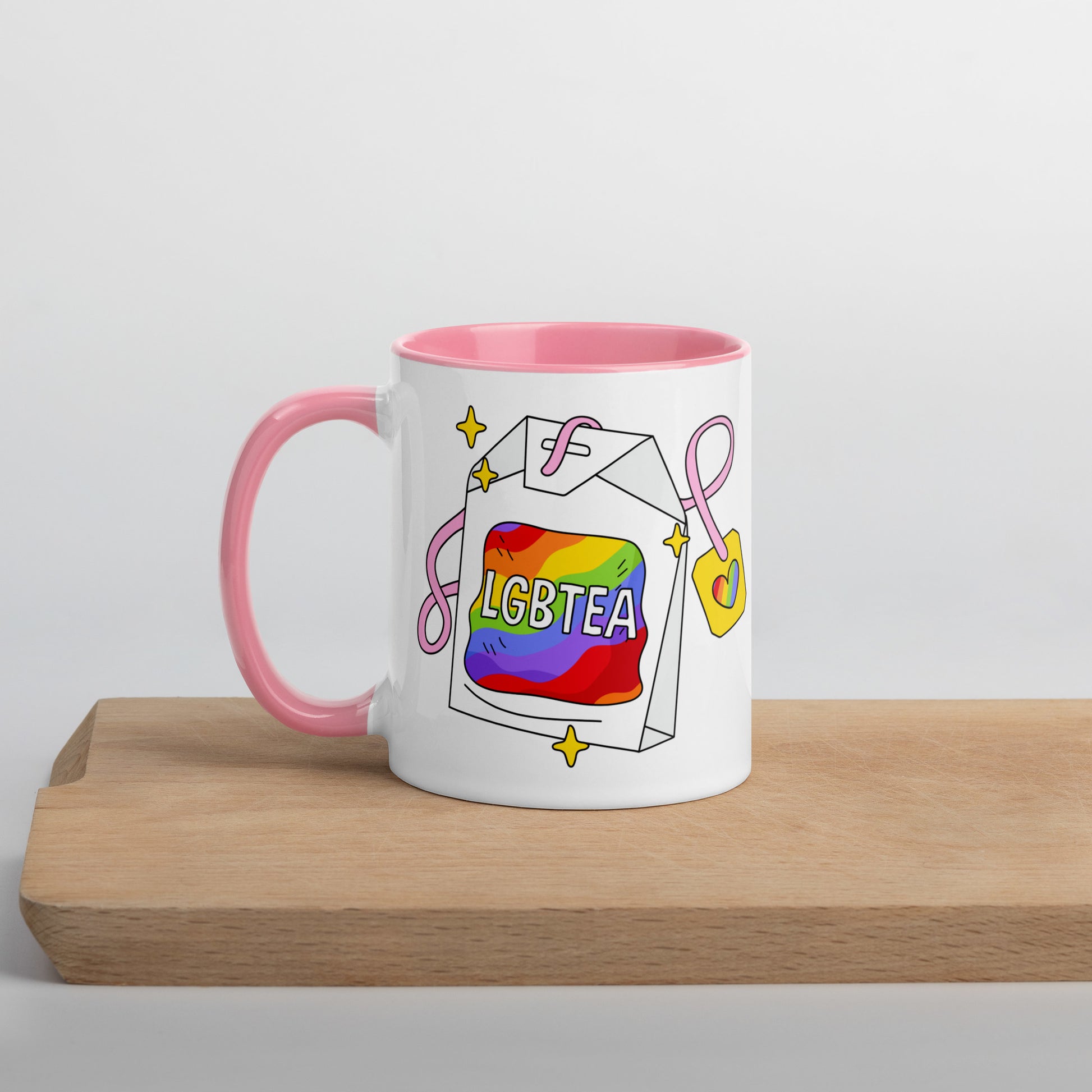 White ceramic 11oz LGBTea mug with pink handle and interior, featuring a rainbow tea bag illustration with pink ribbons and sparkles.