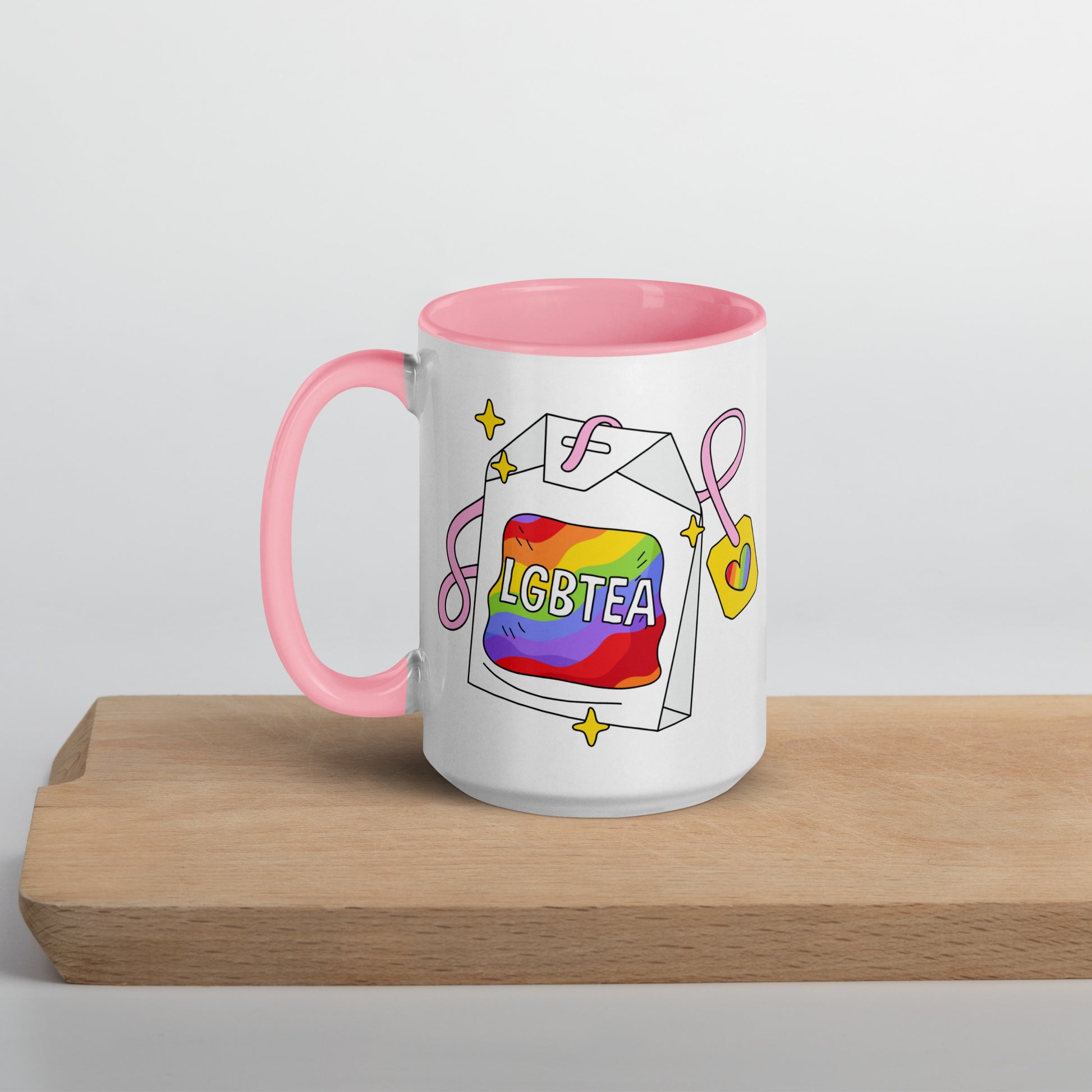 White ceramic 15oz LGBTea mug with pink handle and interior, featuring a rainbow tea bag illustration with pink ribbons and sparkles.