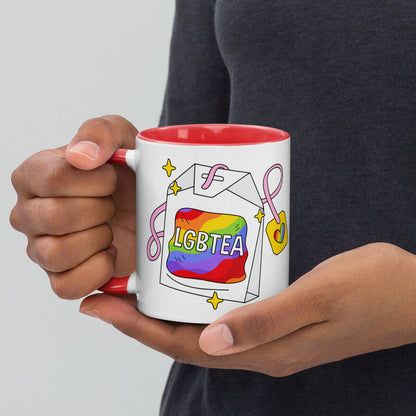 Hands holding a white ceramic LGBTea mug with a red handle and interior, featuring a rainbow tea bag illustration with pink ribbons and sparkles.
