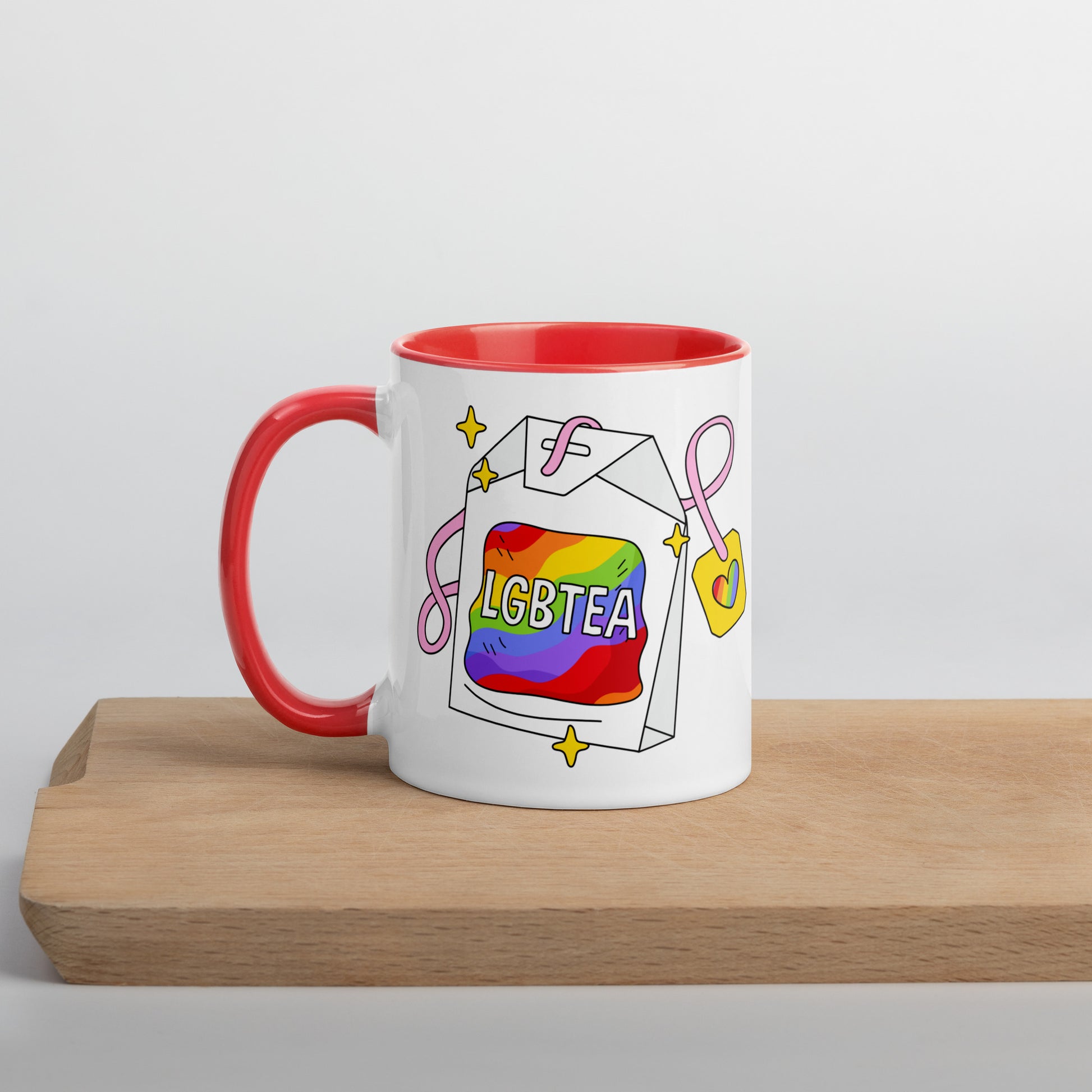 White 11oz ceramic LGBTea mug with red handle and interior, featuring a rainbow tea bag illustration with pink ribbons and sparkles.