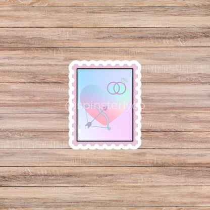 A rectangular scalloped sticker featuring a pastel gradient background with a bow and arrow and two interlocking rings, displayed on a light brown wood plank surface.