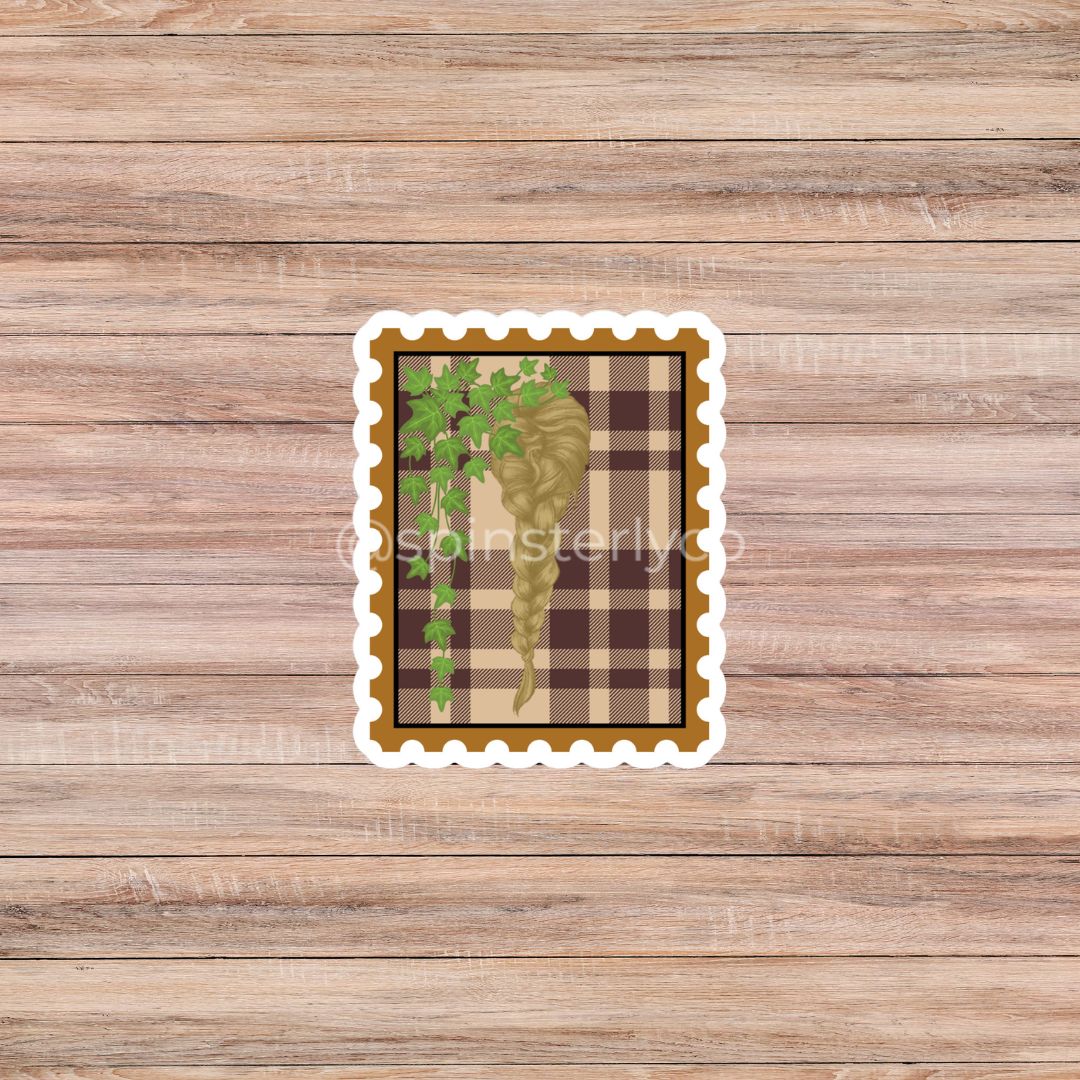A rectangular scalloped sticker featuring a brown and beige plaid background with a green ivy vine and a gold leaf, shown on a light brown wood plank background.