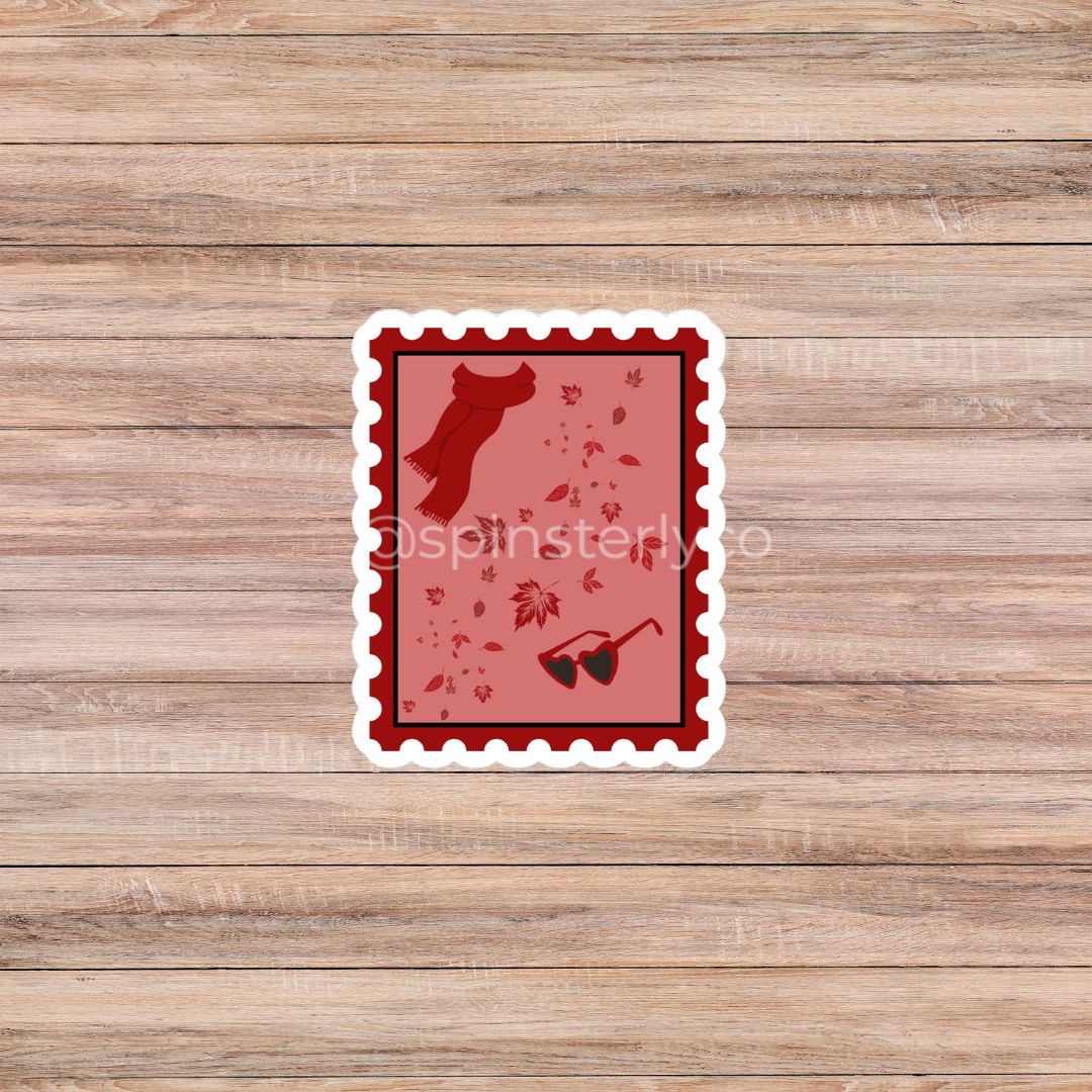 A rectangular die-cut sticker with a scalloped white border, featuring a red and pink autumn-themed design with a silhouette of a dog, scattered leaves, and sunglasses, displayed on a light brown wood plank background.