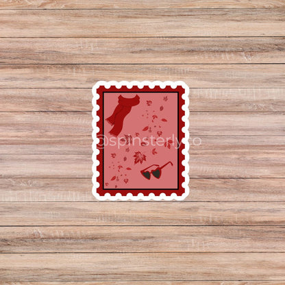 A rectangular die-cut sticker with a scalloped white border, featuring a red and pink autumn-themed design with a silhouette of a dog, scattered leaves, and sunglasses, displayed on a light brown wood plank background.