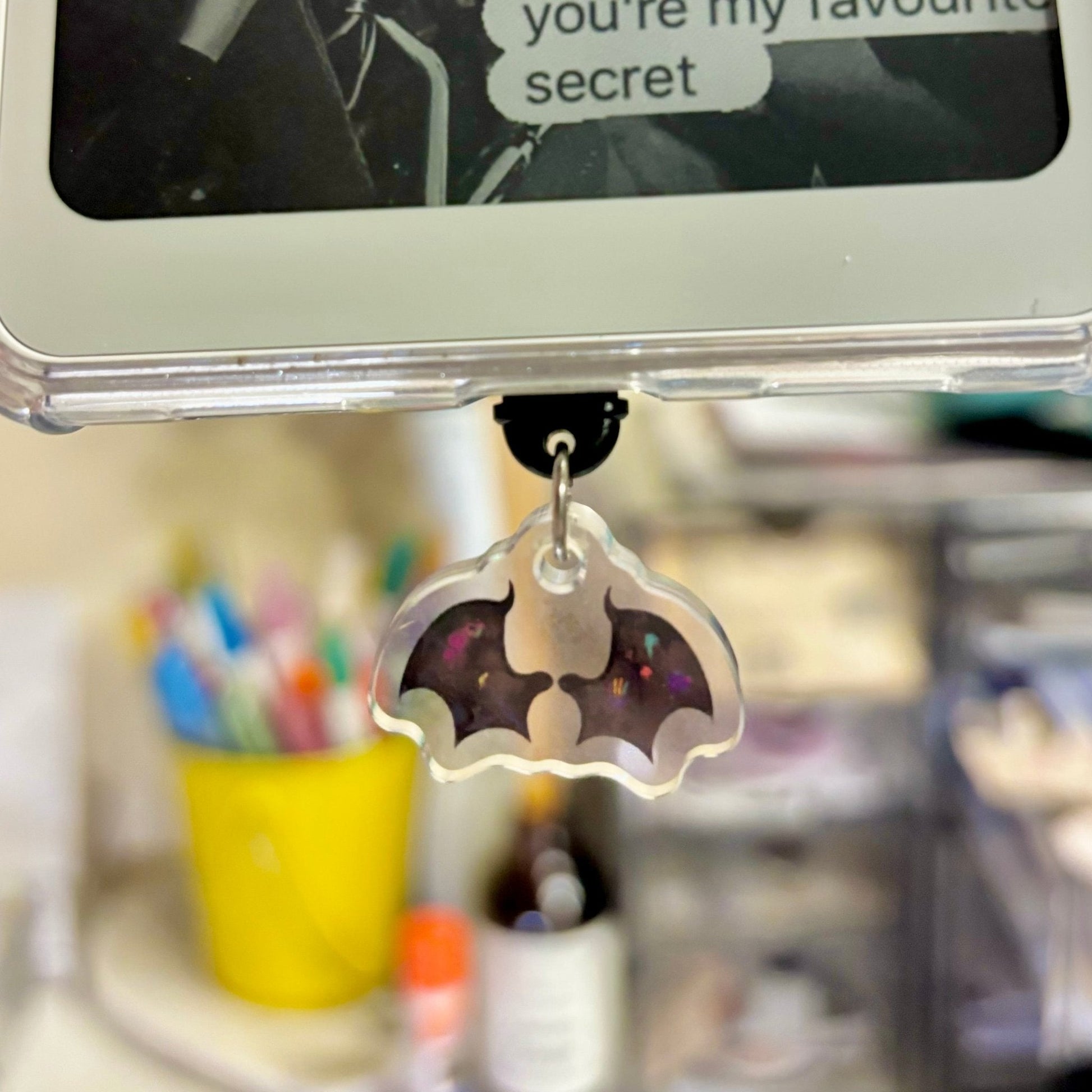 Phone charm shaped like a bat with colorful details on a desk.
