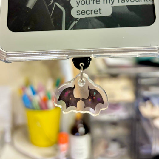 Phone charm shaped like a bat with colorful details on a desk.