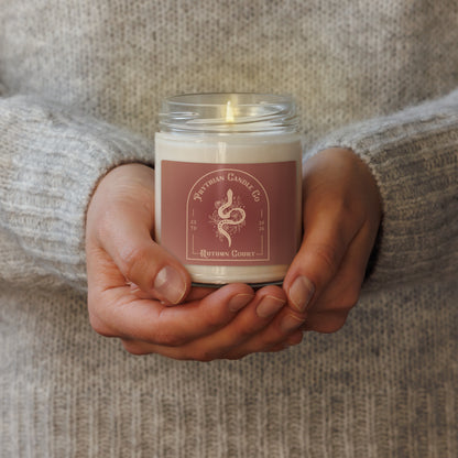 Fae Romantasy Scented Soy Candle by Spinsterly Co in glass jar, lit with warm glow on a sofa