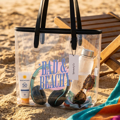 Bad Beachy Clear Tote Bag by Spinsterly Co, transparent waterproof TPU with black handles at the beach