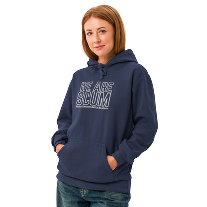 A woman modeling a navy blue pullover hoodie with 'WE ARE SCUM' printed in white outline text on the chest, paired with blue jeans against a plain white background.