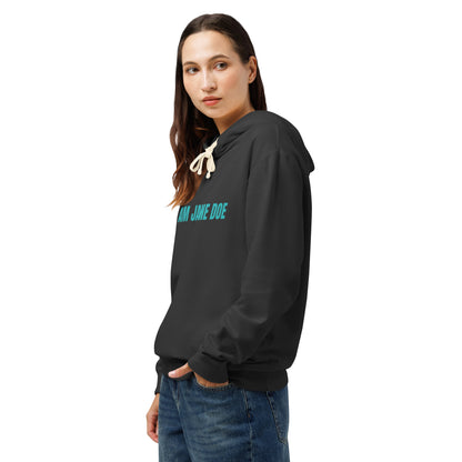 A woman wearing a black pullover hoodie with 'I AM JAME DOE' printed in teal across the chest, paired with blue jeans, shown against a plain white background.