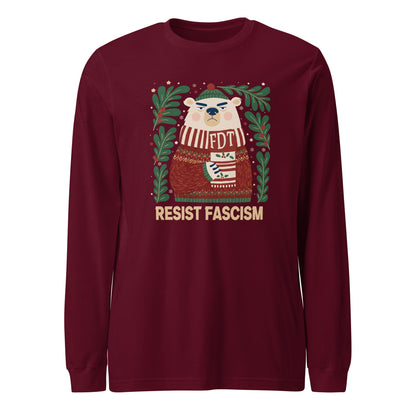 A long-sleeve crewneck t-shirt in maroon, featuring a festive graphic of a polar bear wearing a striped sweater and hat, surrounded by green pine branches, with the text 'RESIST FASCISM' printed below in beige.