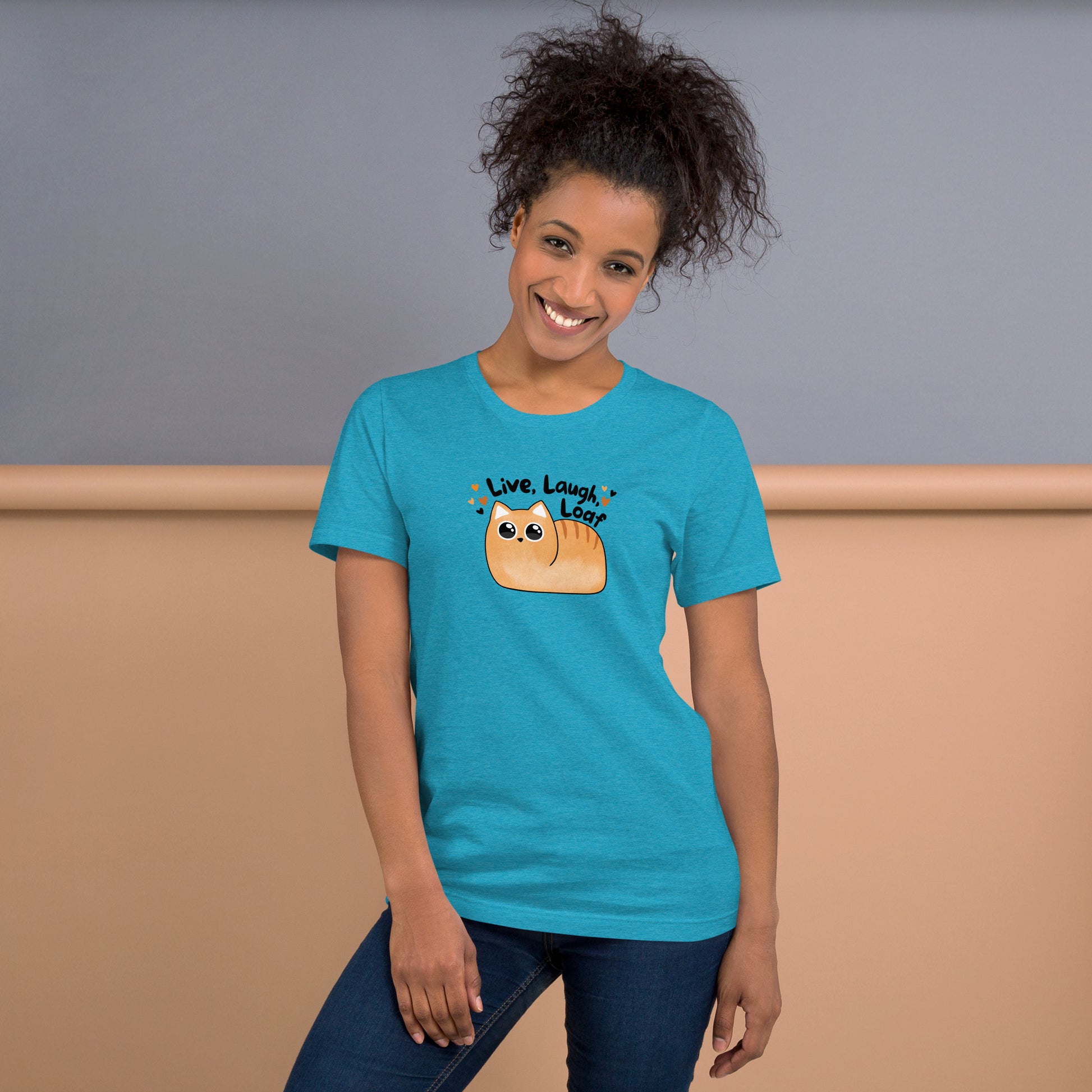 smiling woman with hair up in a messy ponytail wearing the heather aqua t-shirt with kawaii style cat and the phrase live laugh loaf surrounded by tiny hearts.
