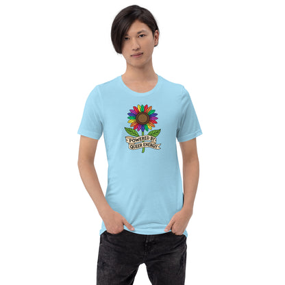 A model wearing a light blue t-shirt with a colorful rainbow sunflower graphic and the text 'POWERED BY QUEER ENERGY' on the chest, paired with black jeans against a plain white background.