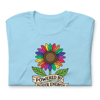 A light blue folded t-shirt featuring a colorful rainbow sunflower graphic with green leaves and a banner that reads 'POWERED BY QUEER ENERGY'.