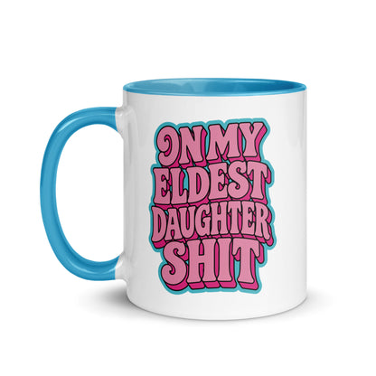 A white ceramic mug with a bright blue handle and interior, featuring the text 'ON MY ELDEST DAUGHTER SHIT' in bold pink bubble letters with a blue outline on the front.