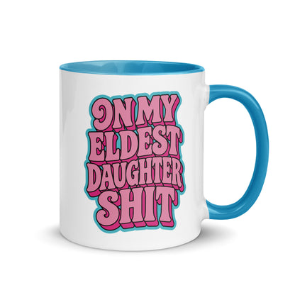 A white ceramic coffee mug with a blue handle and interior, featuring the text 'ON MY ELDEST DAUGHTER SHIT' in pink bubble letters with a teal outline.