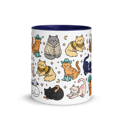 A white ceramic mug with a dark navy blue interior and rim, decorated with a whimsical pattern of illustrated cats in various outfits and poses.