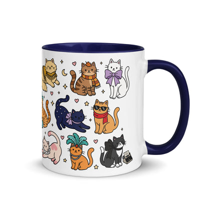 A white ceramic coffee mug with a dark navy blue interior, handle, and rim, decorated with a colorful cartoon pattern of various cats in different poses and outfits.