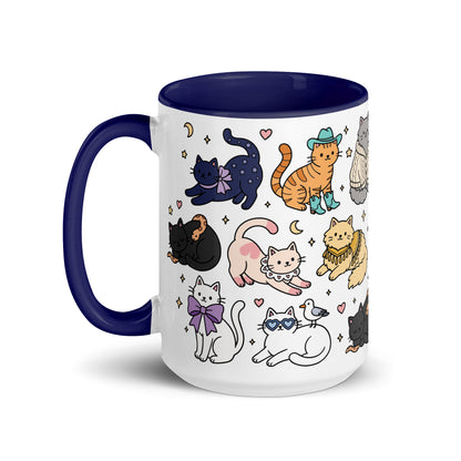 A white ceramic mug with a dark navy blue handle and interior, decorated with a whimsical pattern of various cartoon cats in different poses and outfits.