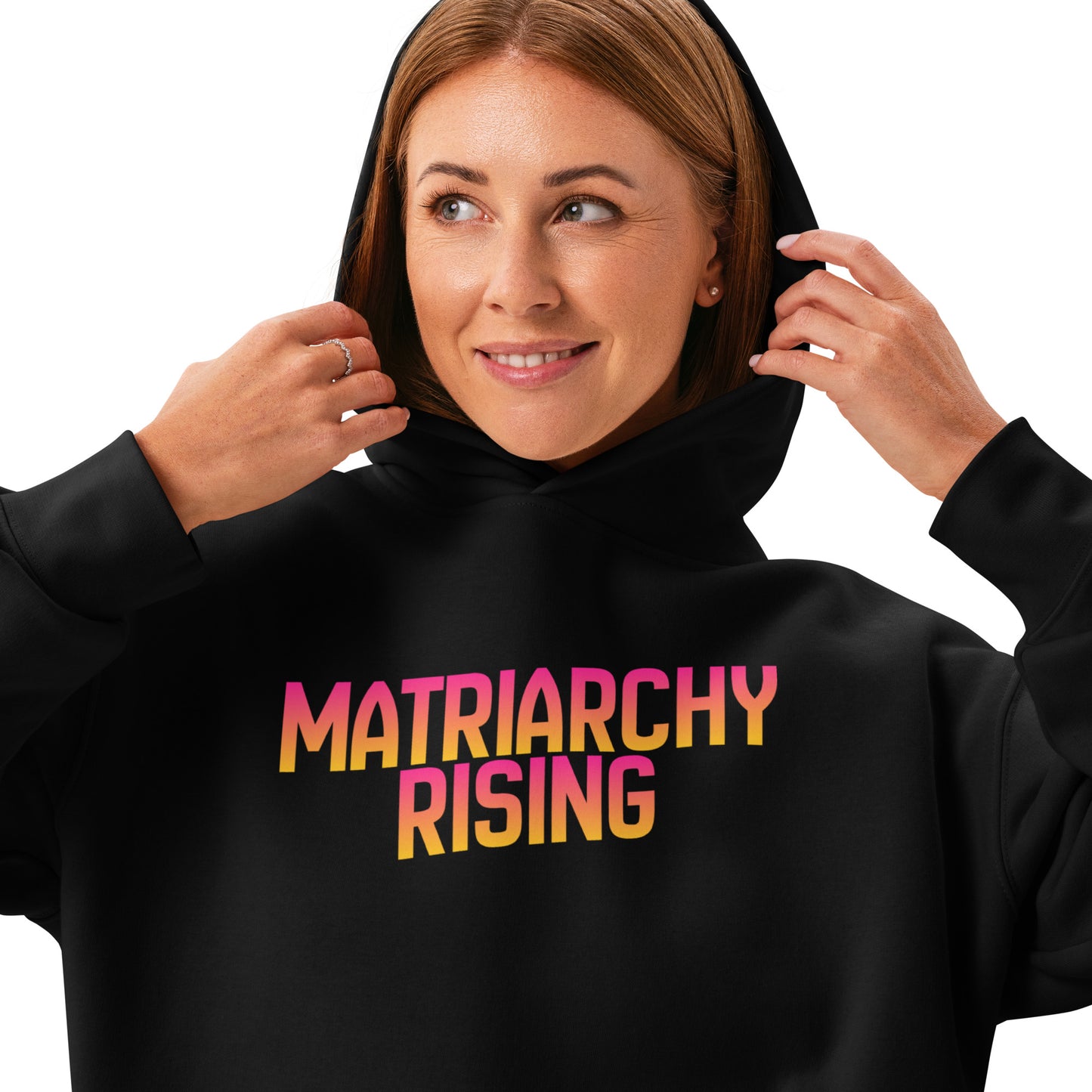 Woman wearing a black Matriarchy Rising hoodie, holding the hood, gradient lettering visible.