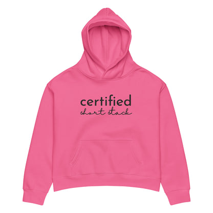 A bright pink cropped hoodie with 'certified short stack' printed in black across the chest, displayed on a clean white background.
